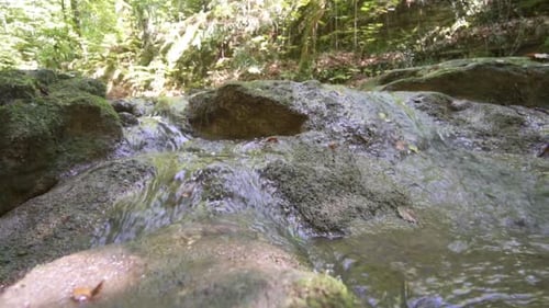 Clean Fresh Water Of Stream Running Over Mossy Rocks During Summer Day.Slow motion pan right.