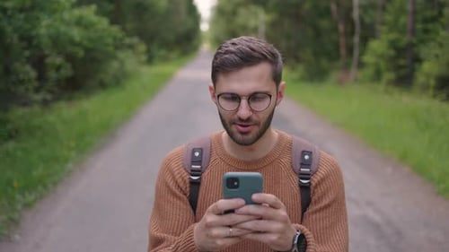 Smiling Man with Glasses with a Beard Walks Through the Woods with a Backpack and Prints a Message