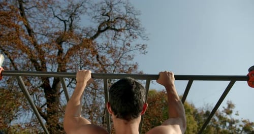Junger Mann macht bei sonnigem Wetter Klimmzüge an der Bar