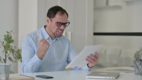 Man Angrily Shakes Documents at Office Desk