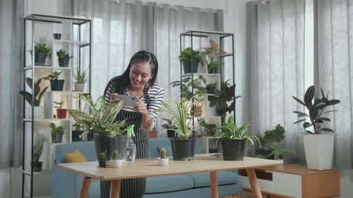 Woman Sprays and Photographs House Plants Indoors