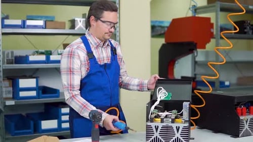 Junge Arbeiterin in Hemd und Overall montiert Elektronisch Komponenten in einer High-Tech-Fabrik