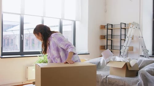 Young Woman Packing Box with Picture Frames Indoors