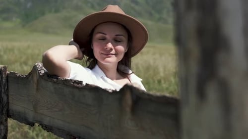 Woman in Hat Resting on Rural Fence
