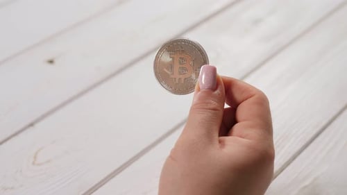 Junge Trader-Investorin hält silberne Bitcoin auf hellem Holzgrund