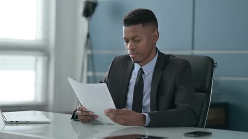 African Businessman Upset while Reading Documents in Office