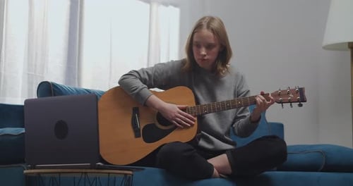 Young Adult Learning Guitar at Home with Laptop