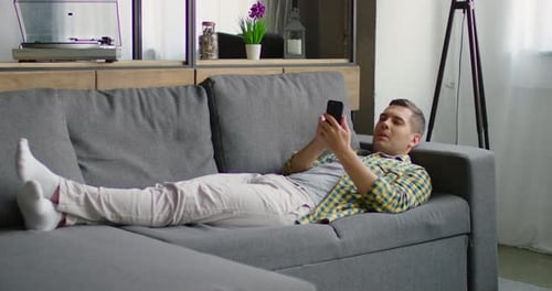 Man Relaxes on Couch Looking at Cellphone