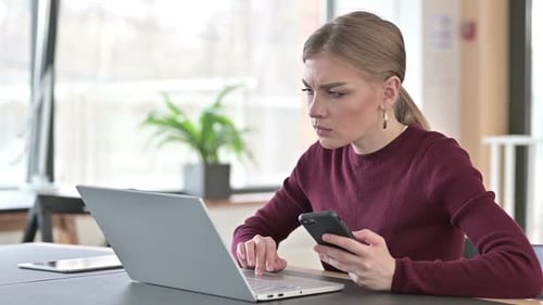 Young Woman Using Laptop and Smartphone in Office