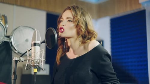 Young female singer recording album in the professional studio.