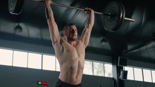 Junger männlicher Athlet hebt eine Langhantel über den Kopf, Krafttraining