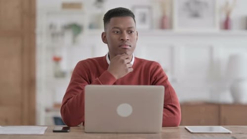 African Man Thinking while Working on Laptop in Office