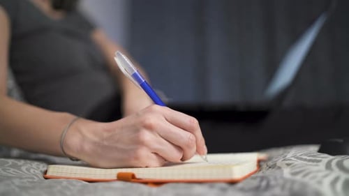 Woman Writing in Notebook with Laptop Computer