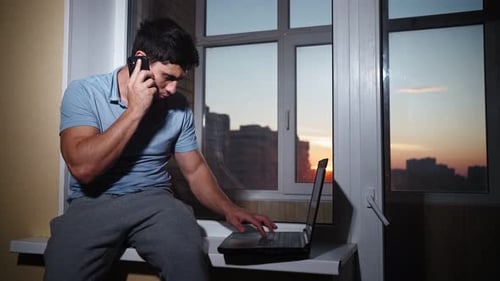 Hombre autónomo trabaja de forma remota en casa mientras está sentado en el alféizar de la