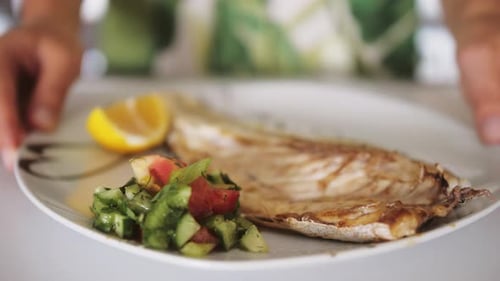 Close Up of Hands Services Plate with Baked Sea Bass Fillet and Salad