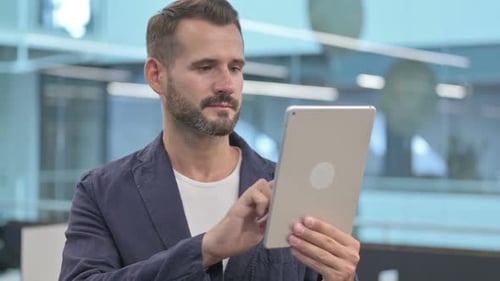 Middle Aged Businessman Browsing Internet on Tablet in Office