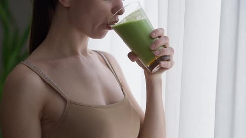 Unrecognizable Woman Looking Out Window Drinking Healthful Green Smoothie Smiling