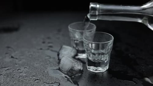 Pouring Up Shots of Vodka From a Bottle Into Glass. Black Background