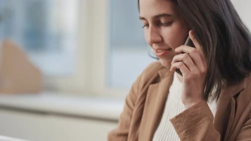 Woman Using Laptop and Talking on Smartphone in Office