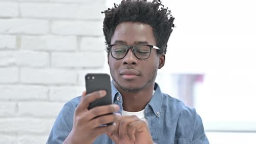 Young Man Uses Smartphone Smiling Indoors
