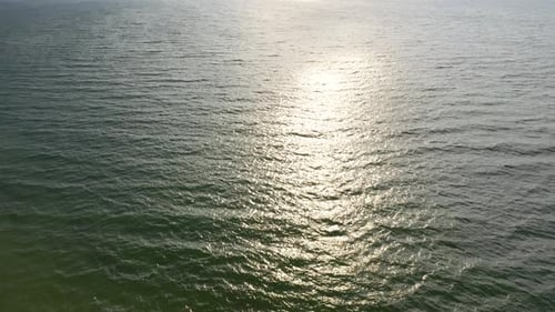 AERIAL: Locked Shot of Waves Crashing on the Surface of Reflective Sea