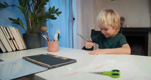 Cute Child Boy Drawing with Pencil Sitting at the Table on Living Room