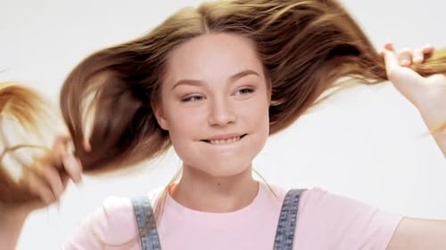 Junges schönes Mädchen, das lächelt und tanzt und Haare auf weißem Hintergrund hält