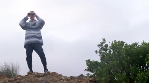 Adventurer With Binoculars Standing on Rocky Hill