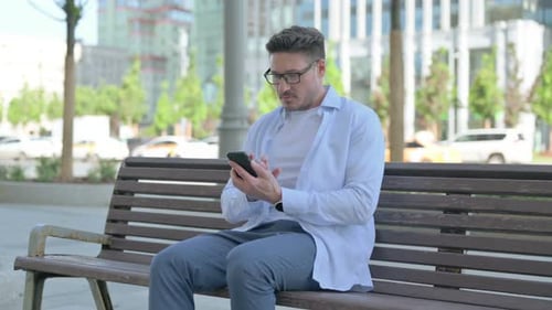 Man Using Smartphone While Sitting on Park Bench