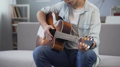 Adolescent de sexe masculin apprenant à jouer de la guitare assis dans sa chambre, pratiquant