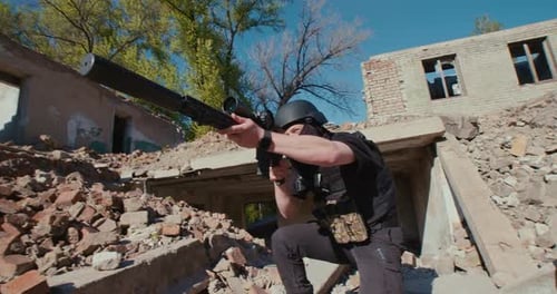 Un soldat armé sort de la maison détruite et tire