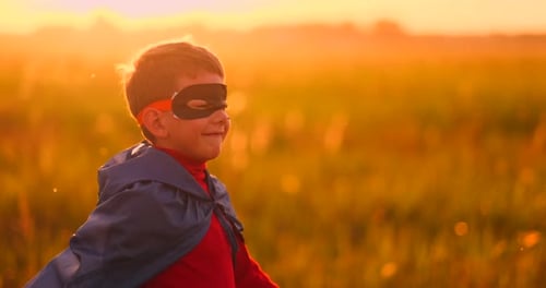 The Boy in the Mask and Cape of a Super Hero at Sunset in a Field