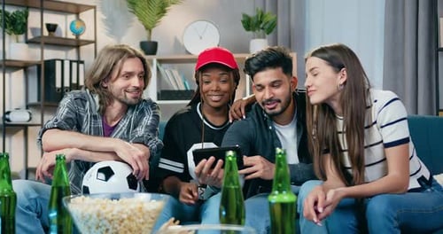 Jóvenes mestizos sentados en el sofá de casa y usan el teléfono inteligente para ver videos divertidos