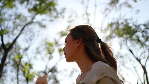4K Asian woman drinking water from a bottle while jogging at public park in the morning.