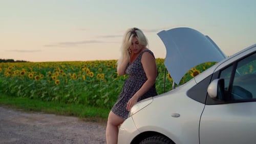 Woman talking service by phone looking in car engine on rural road. Attractive 30s Girl has trouble