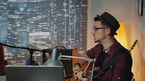 Profile View of Handsome Hipster Singing Into Microphone and Playing the Guitar in Home Recording