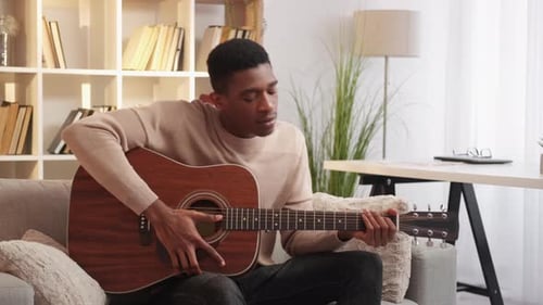 Young Adult Playing Acoustic Guitar on Sofa
