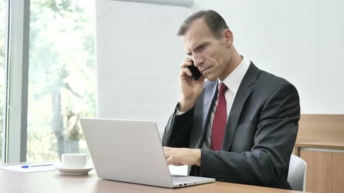 Businessman Talking on Phone and Using Laptop