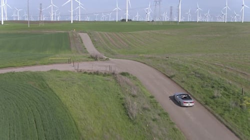 Car Driving On The Dirt Road Among Windmills