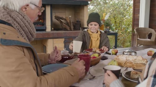 Family and Child Have Tea at Table Outdoors