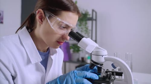 Focused Scientist Examining Sample Under Microscope in Lab