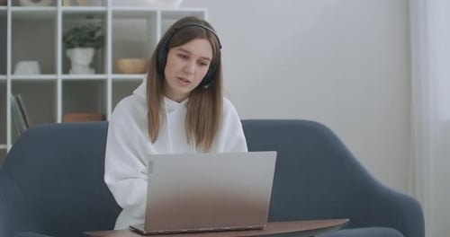 Young Woman in Hoodie Using Laptop with Headphones