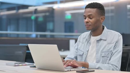 Young Man Smiling and Typing on Laptop in Office