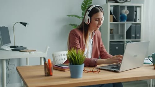 Woman Working on Laptop Wearing Headphones in Office