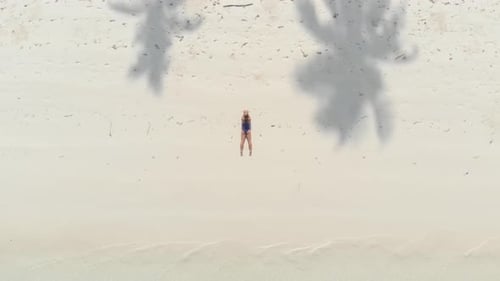 Aerial: Woman relaxing on white sand beach turquoise water tropical coastline