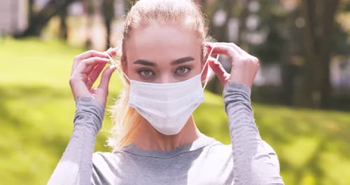 Woman Puts on Surgical Face Mask Outdoors