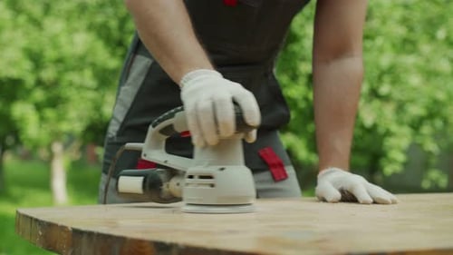Nahaufnahme Männlicher Zimmermann poliert einen Holztisch mit einer Schleifmaschine