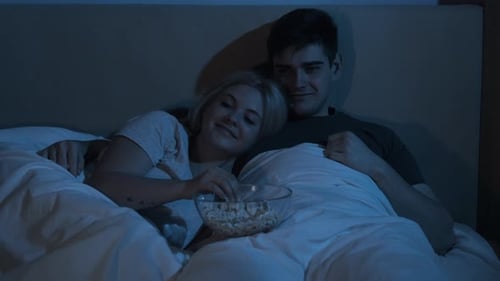 Loving Couple Eating Popcorn in Bed at Night