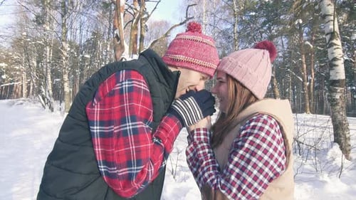 Beautiful Couple of Smiling Young People in a Snowy Forest on a Sunny Day Warming Their Hands with