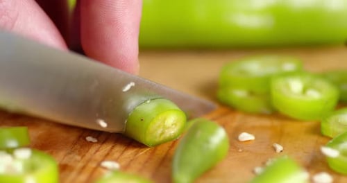 Hands of a Man with a Knife Cut the Green Chili Peppers.